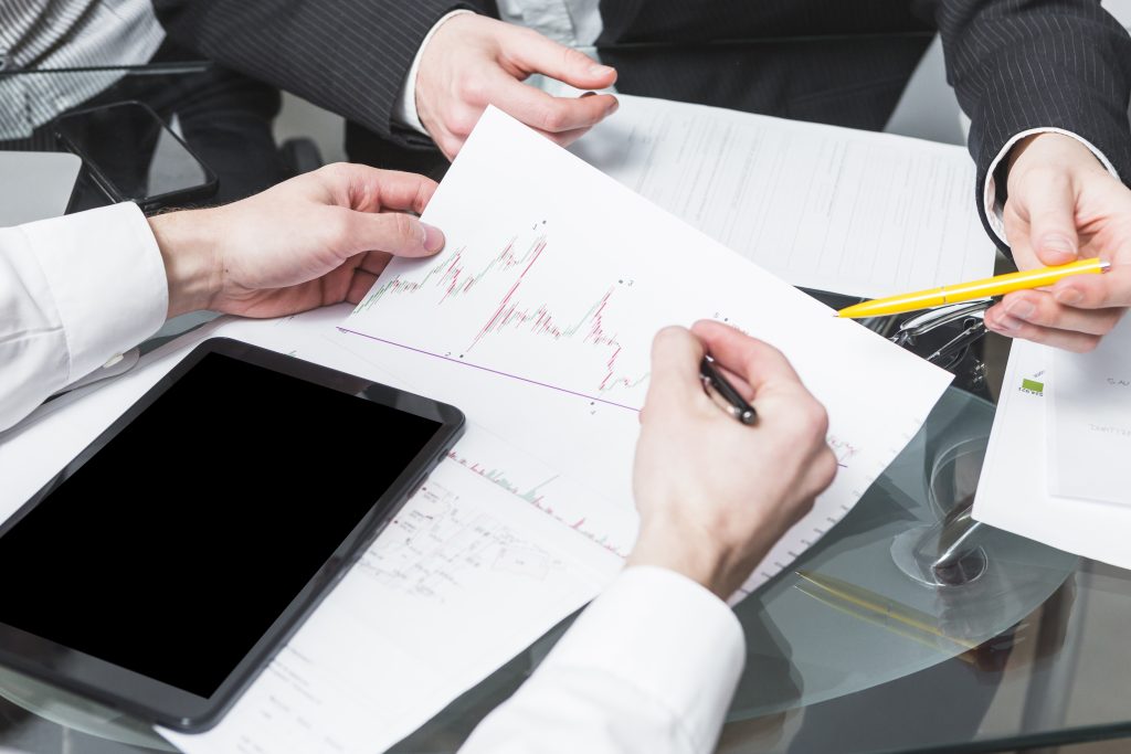 Hände von zwei Personen, die mit Zetteln und Papier eine Bilanz analysieren